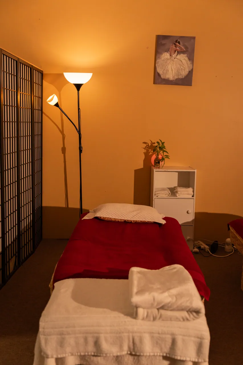 A cozy massage bed beside a warm lamp and a flower arrangement
